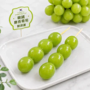 兩支甜一口糖葫蘆的韓國麝香葡萄糖葫蘆,擺放在白色方形餐盤上,旁邊附有韓國麝香葡萄糖葫蘆的品牌小立牌。